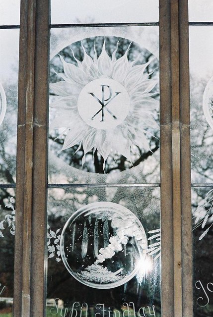 Detail of a Laurence Whistler engraved glass window, with a radiant Christian monogram and a delicate globe of natural forms
